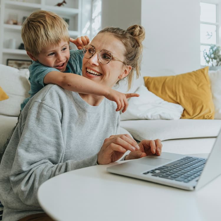 Eine Frau sitzt am Laptop, ihr Sohn umarmt sie und zeigt auf den Bildschirm