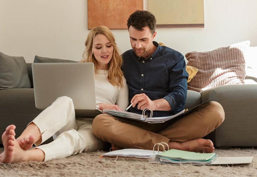 Ein junges Paar sitzt mit Aktenordner und Laptop auf dem Boden vor der Couch