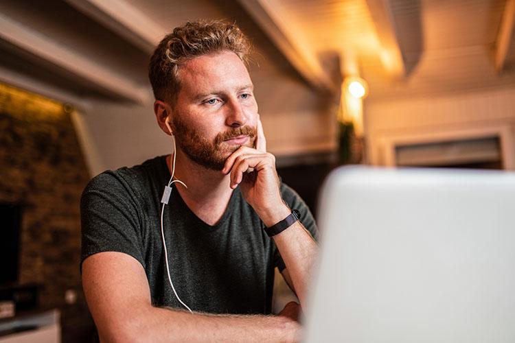 Mann mit Kopfhörern im Ohr schaut auf Laptop