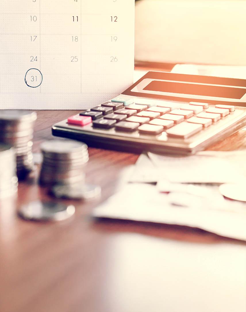 Taschenrechner inmitten von Kleingeld vor einem Kalender, in dem der 31. umkreist ist.