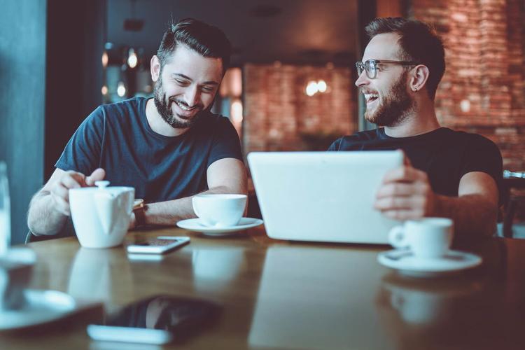 Zwei Männer im Café lachend am Laptop.