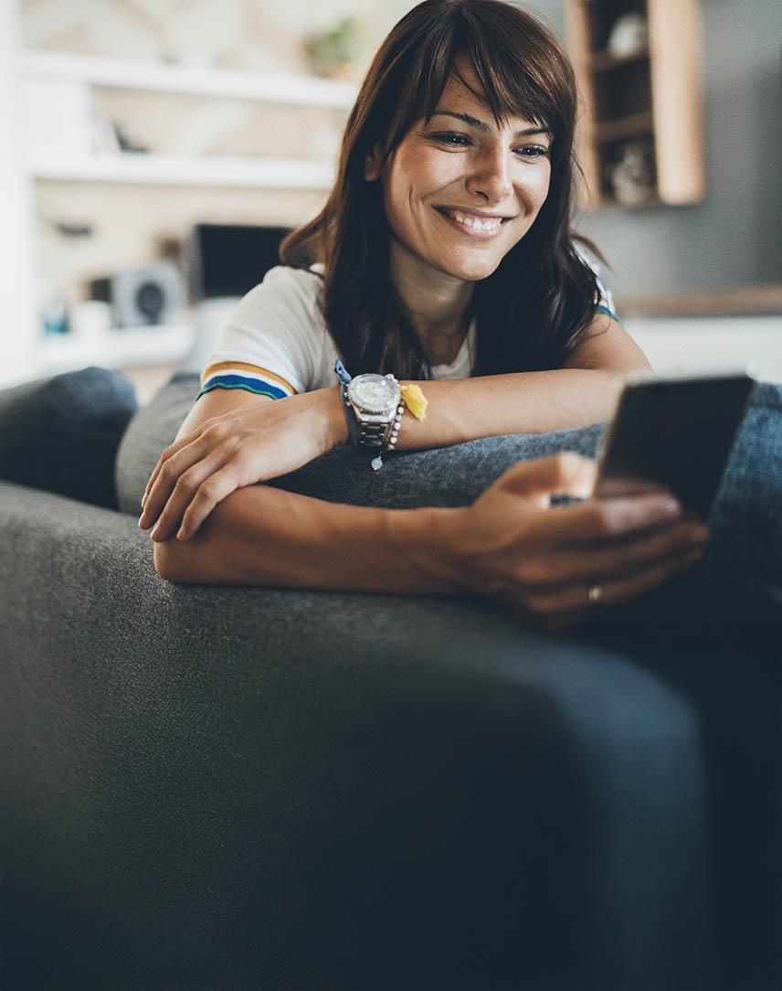 Frau schaut in ihrem Zuhause lächelnd auf ihr Smartphone