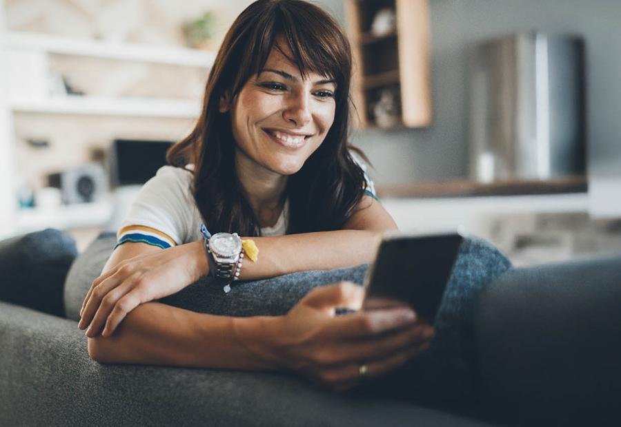 Frau schaut in ihrem Zuhause lächelnd auf ihr Smartphone