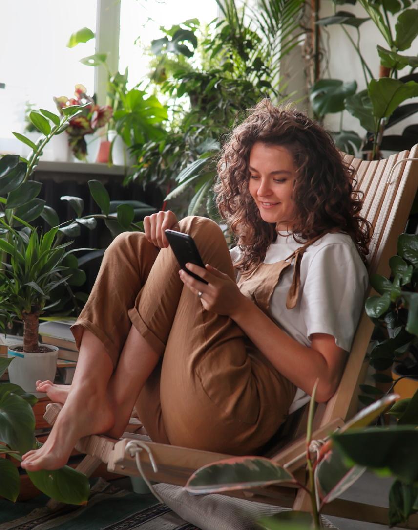 Junge Frau schaut inmitten vieler Grünpflanzen auf ihr Smartphone