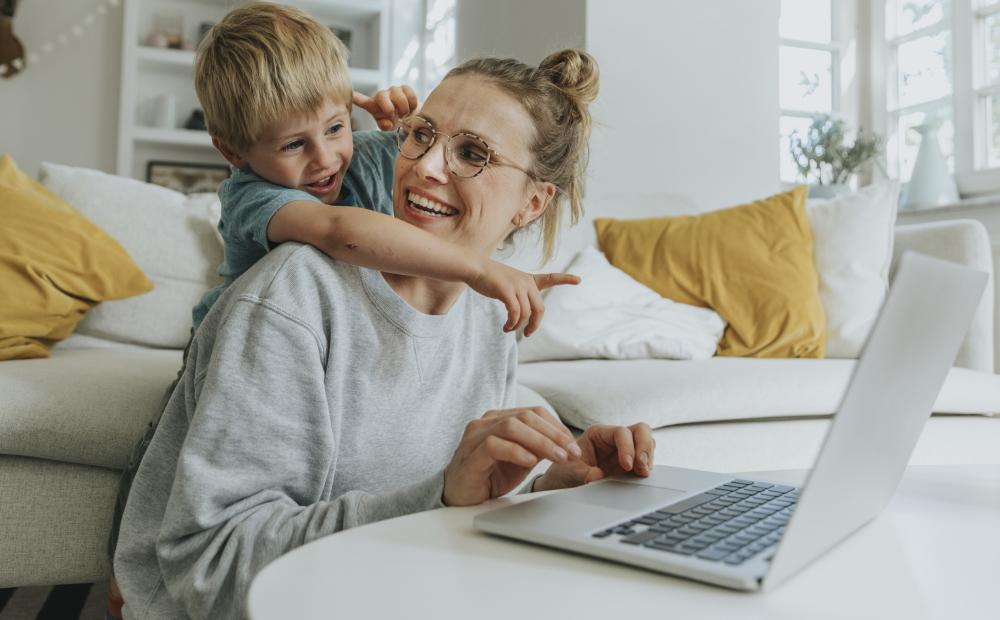 Eine Frau sitzt am Laptop, ihr Sohn umarmt sie und zeigt auf den Bildschirm