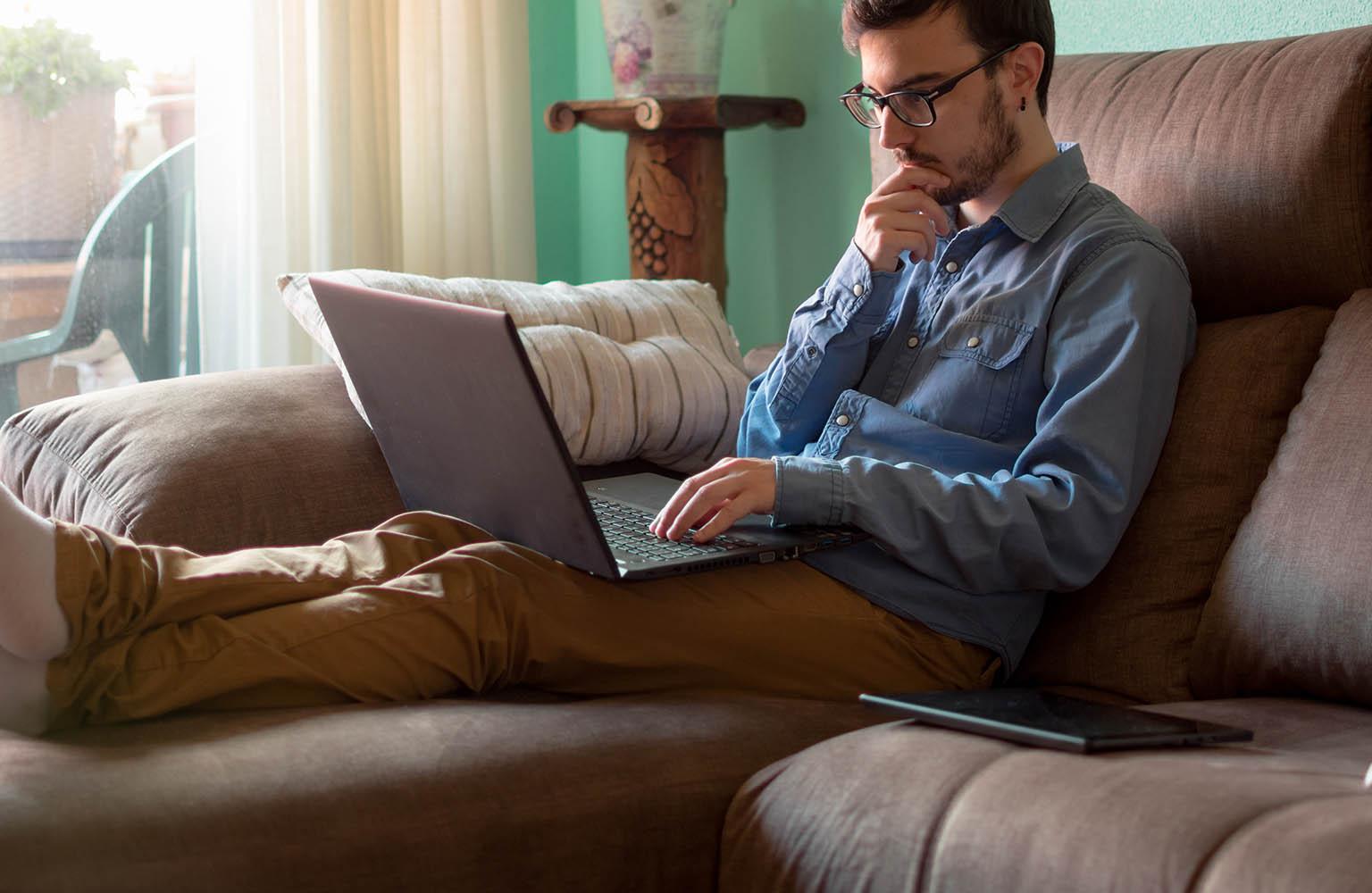 Mann sitzt auf der Couch mit Laptop und informiert sich 
