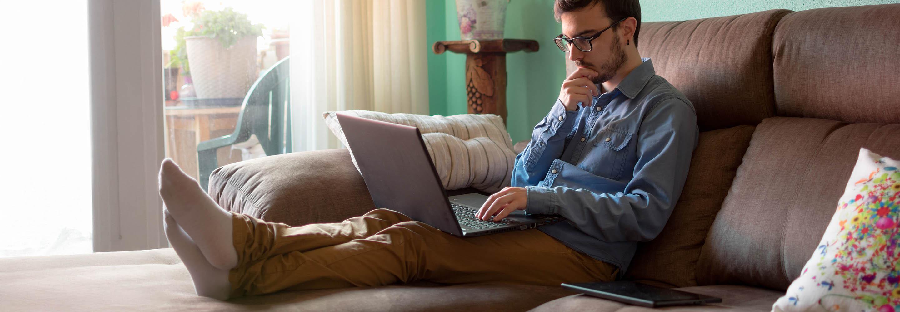 Mann sitzt auf der Couch mit Laptop und informiert sich 
