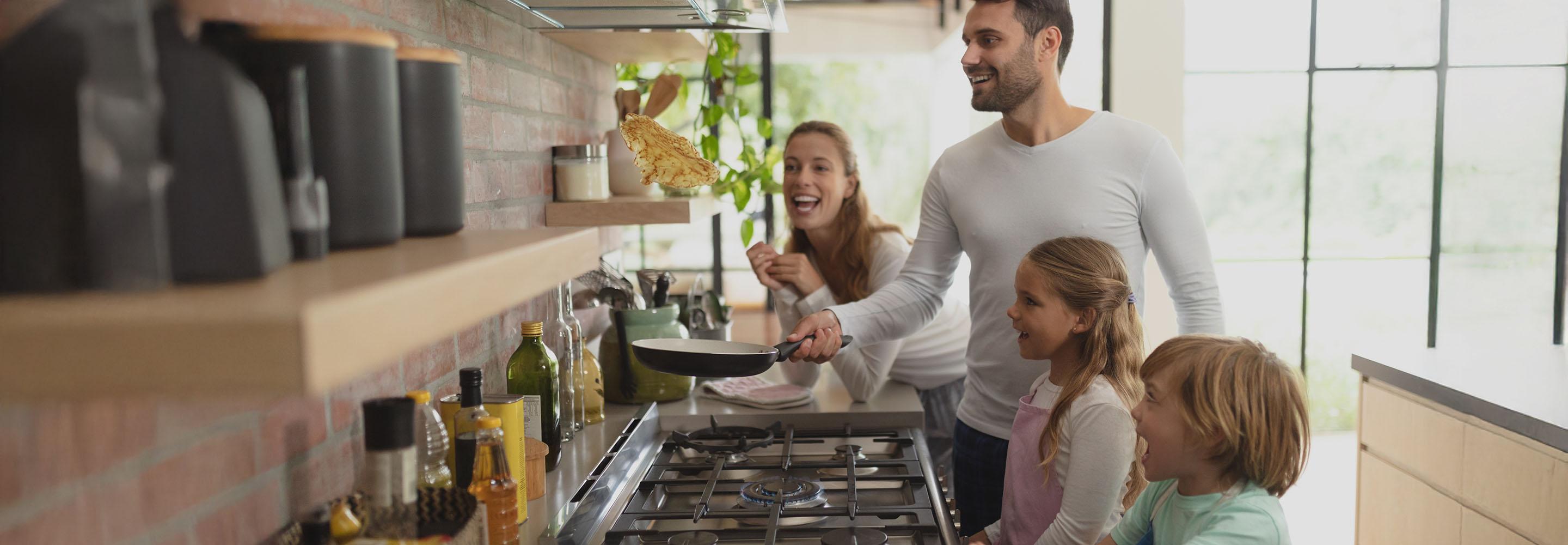 Familie steht am Gasherd, der Vater wirft einen Pfannkuchen aus der Pfanne durch die Luft