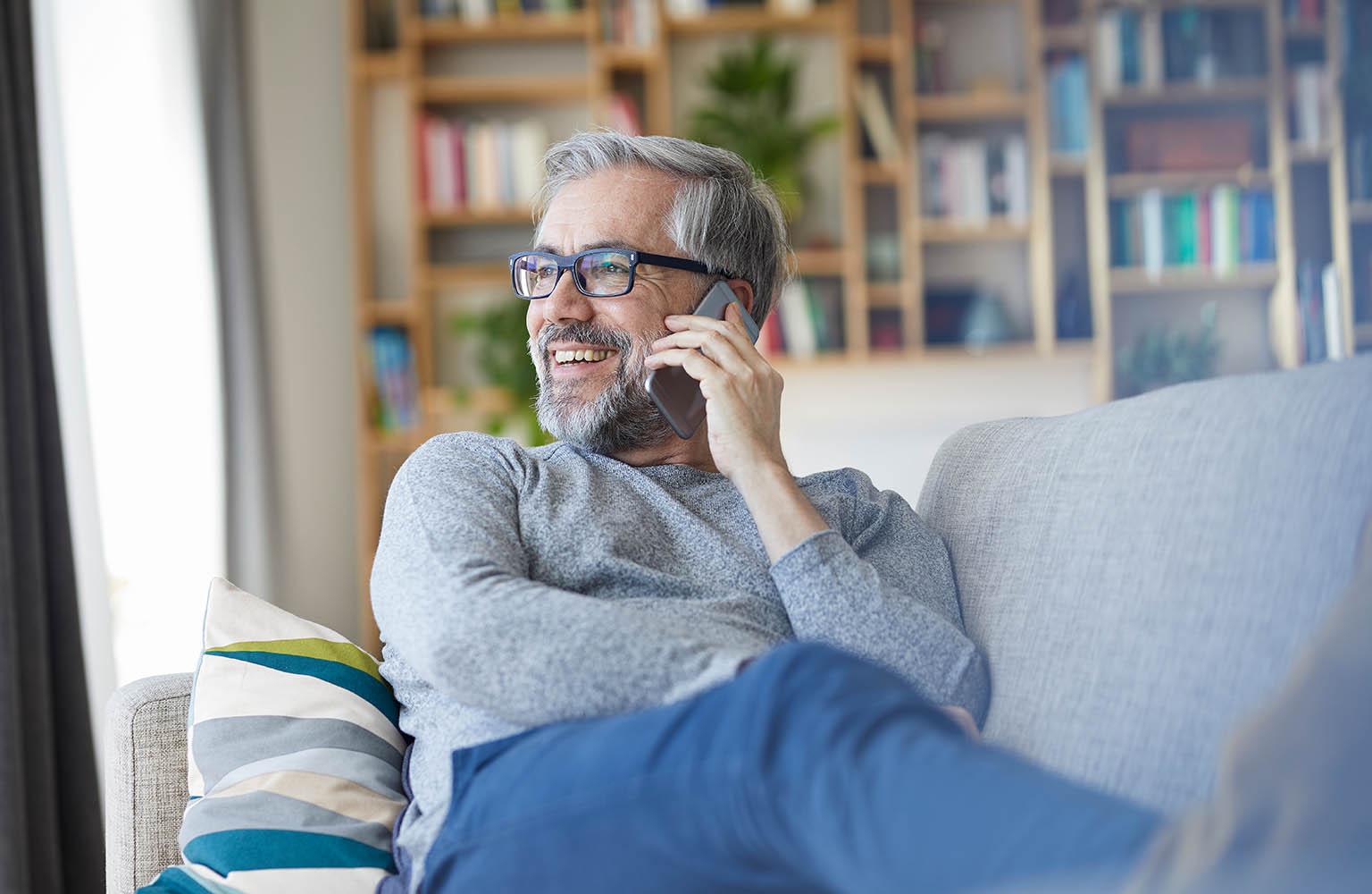Mann auf dem Sofa telefoniert mit dem Smartphone.