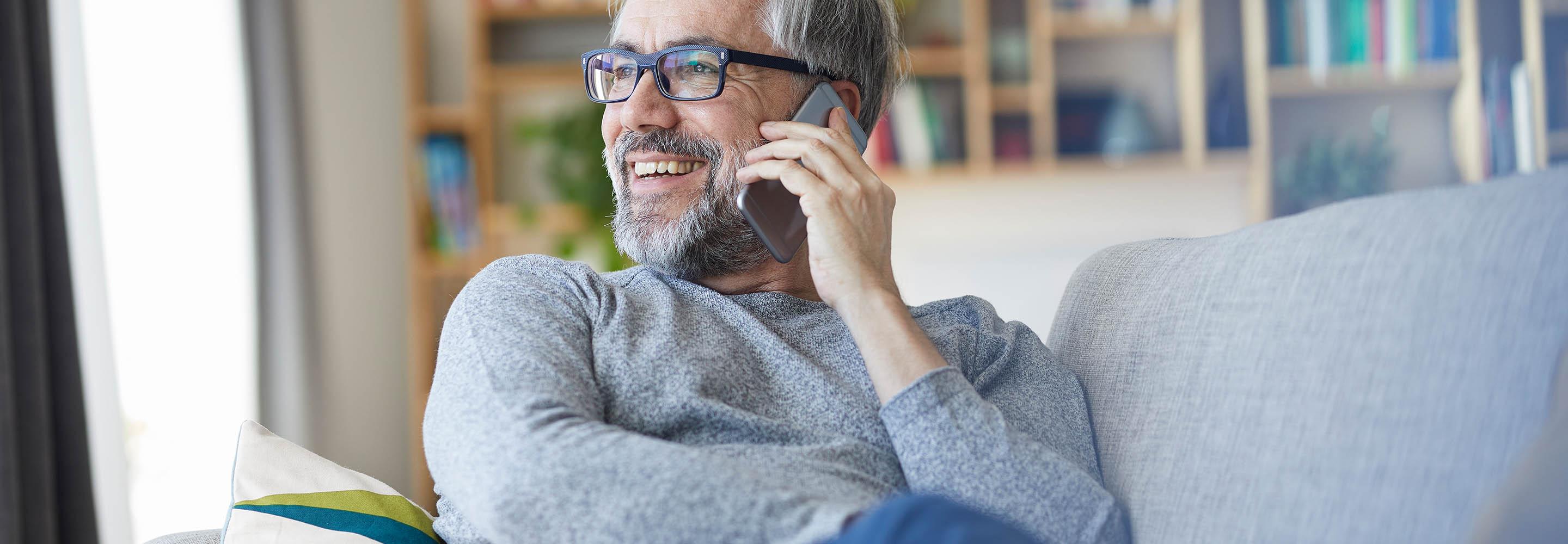 Mann auf dem Sofa telefoniert mit dem Smartphone.