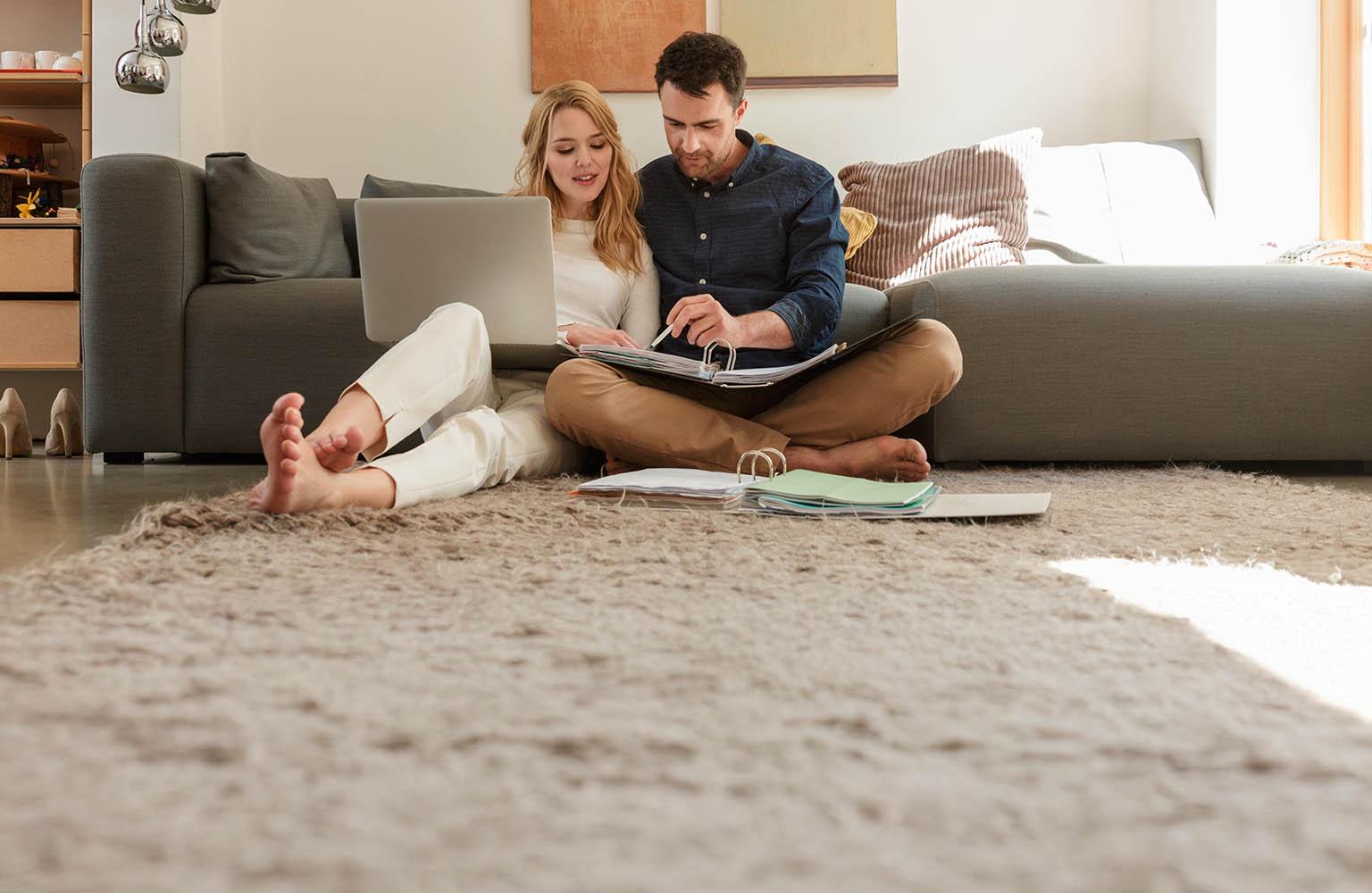 Ein junges Paar sitzt mit Aktenordner und Laptop auf dem Boden vor der Couch