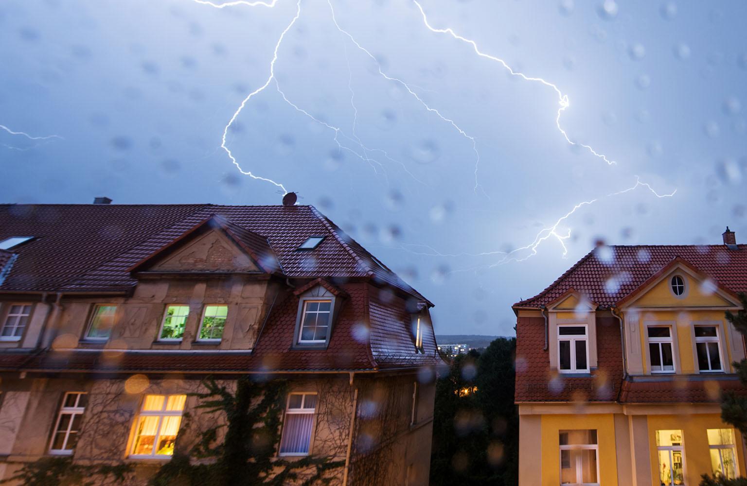 Blitze am verregneten Himmel über Häuserreihe