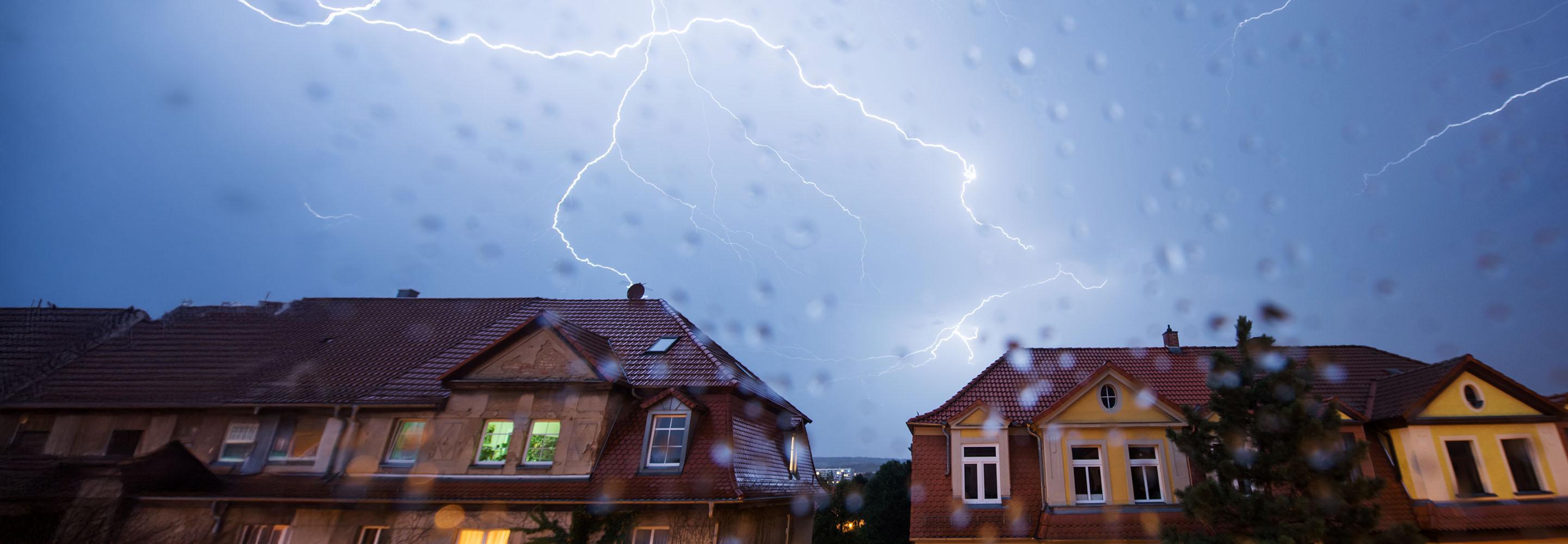 Blitze am verregneten Himmel über Häuserreihe