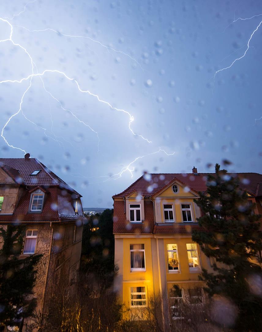 Blitze am verregneten Himmel über Häuserreihe