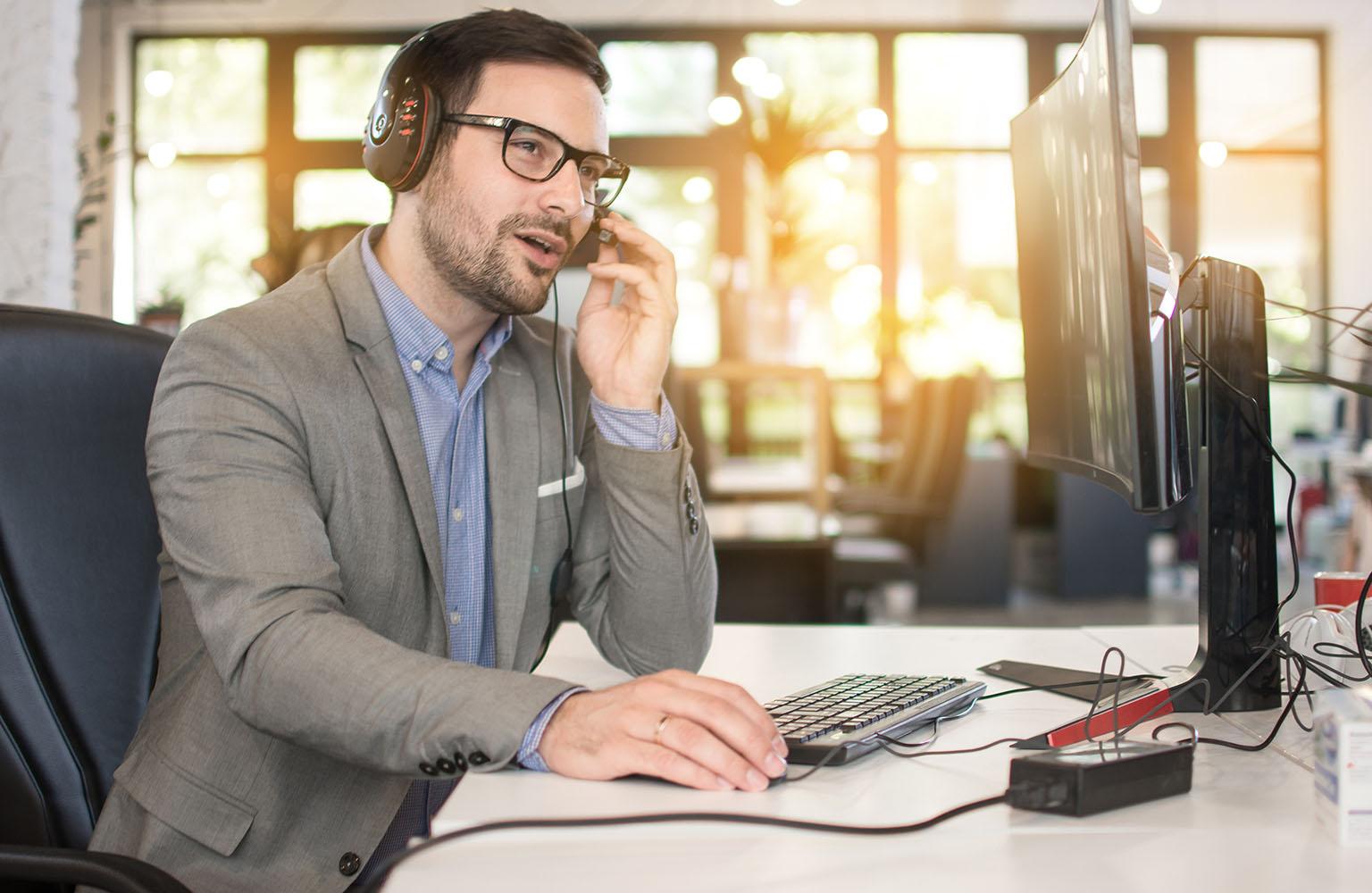 Mann mit Headset sitzt am Schreibtisch und spricht.
