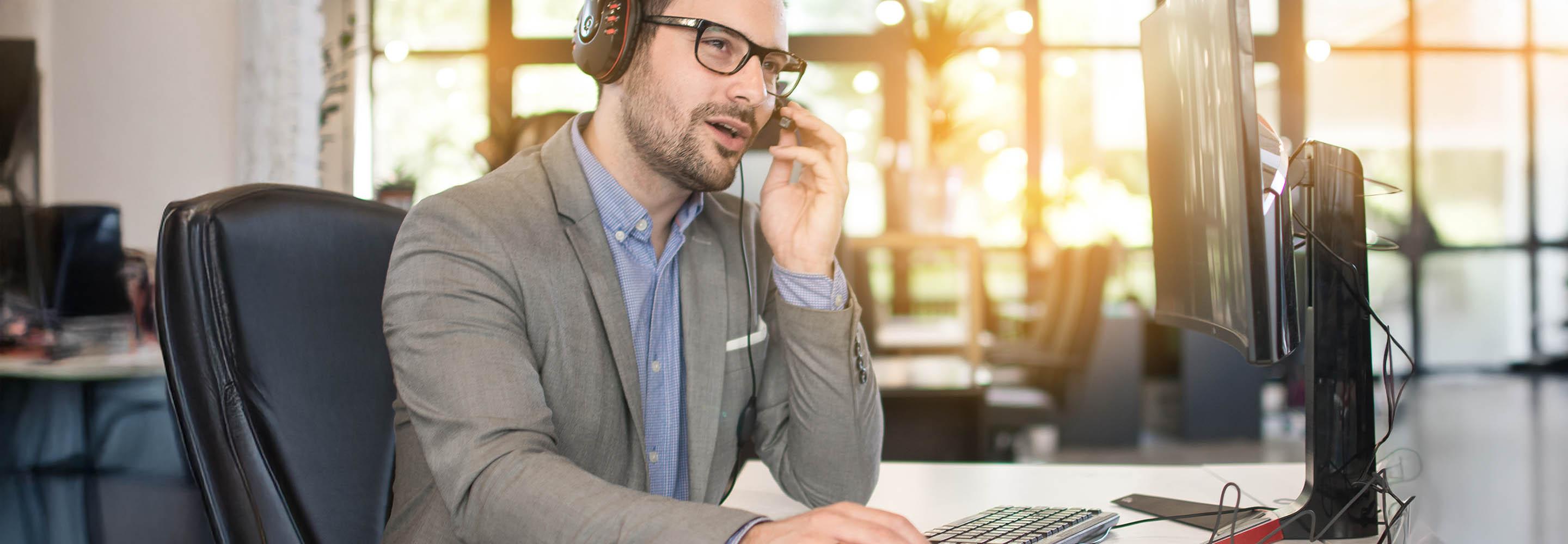 Mann mit Headset sitzt am Schreibtisch und spricht.
