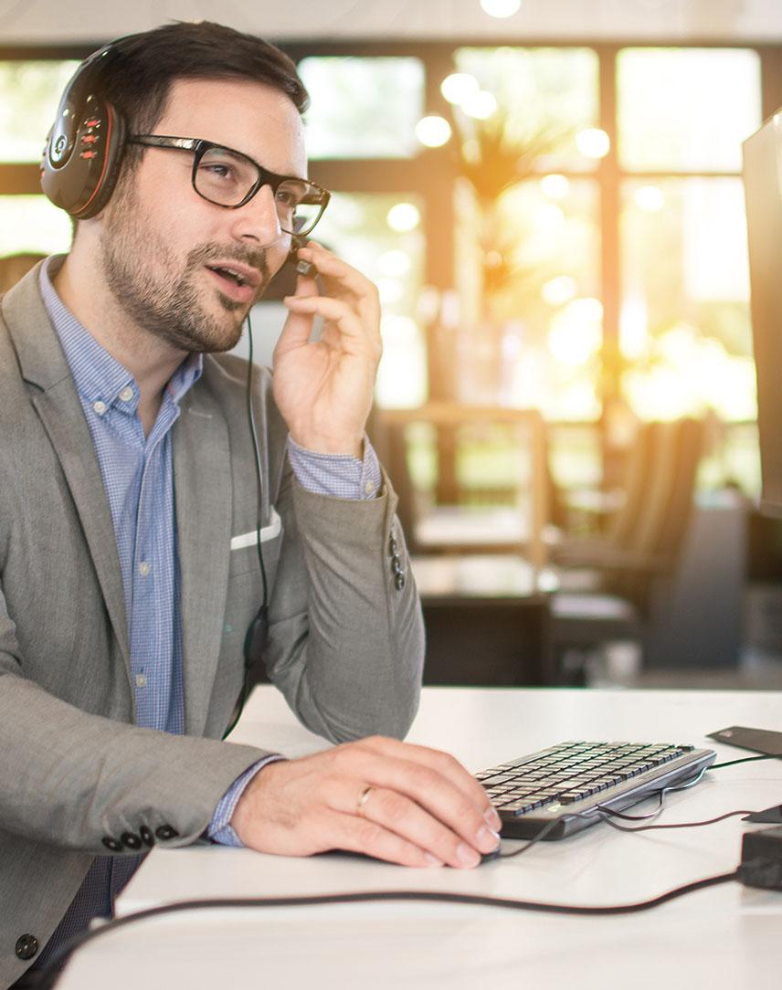 Mann mit Headset sitzt am Schreibtisch und spricht.