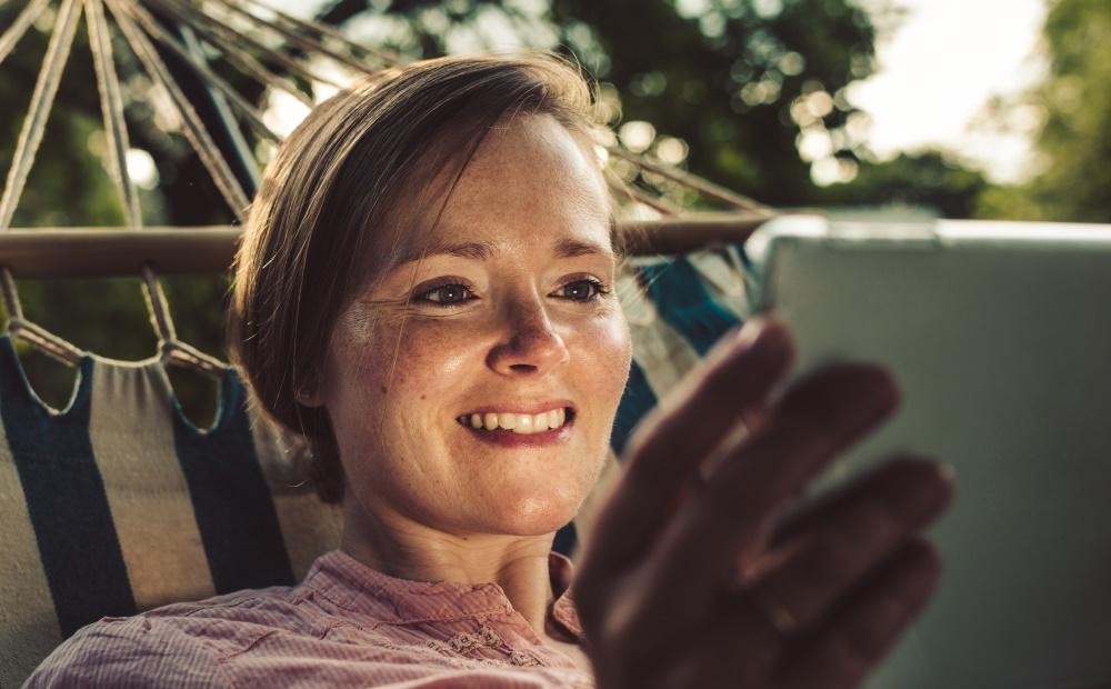 Frau in Hängematte liegend schaut aufs Tablet.