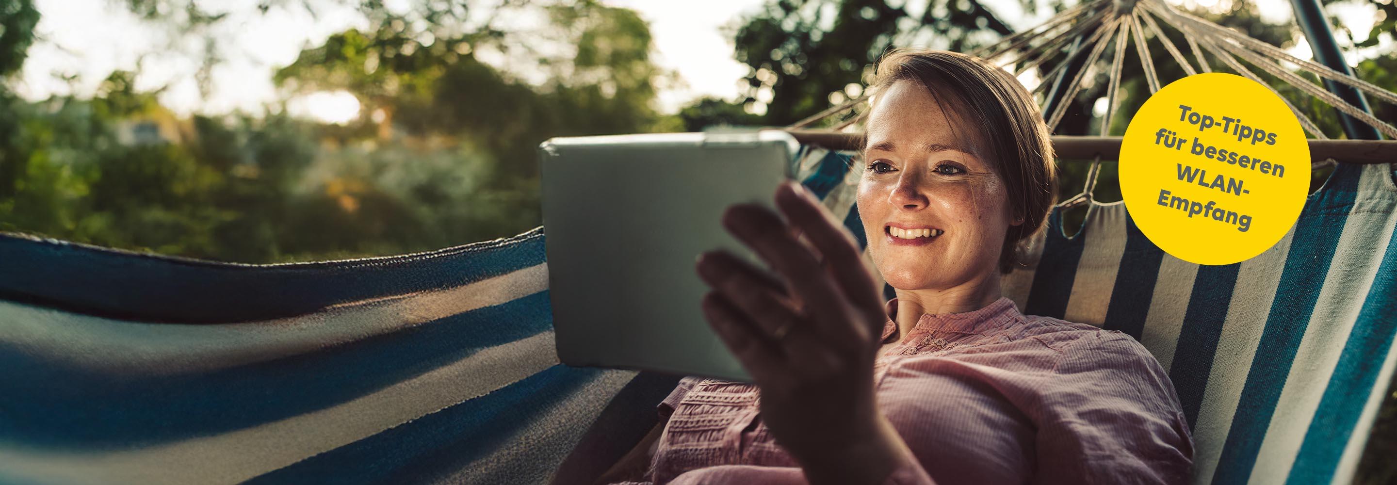 Frau in Hängematte liegend schaut aufs Tablet.