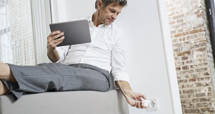 Mann lädt sein Tablet an einer Steckdose auf
