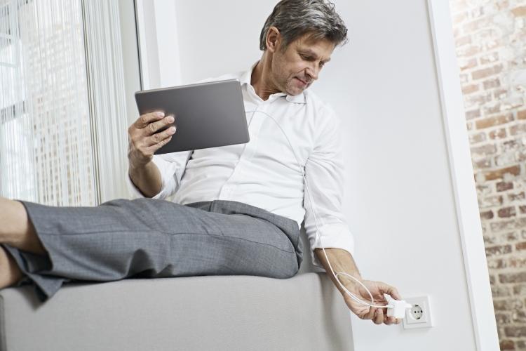 Mann lädt sein Tablet an einer Steckdose auf