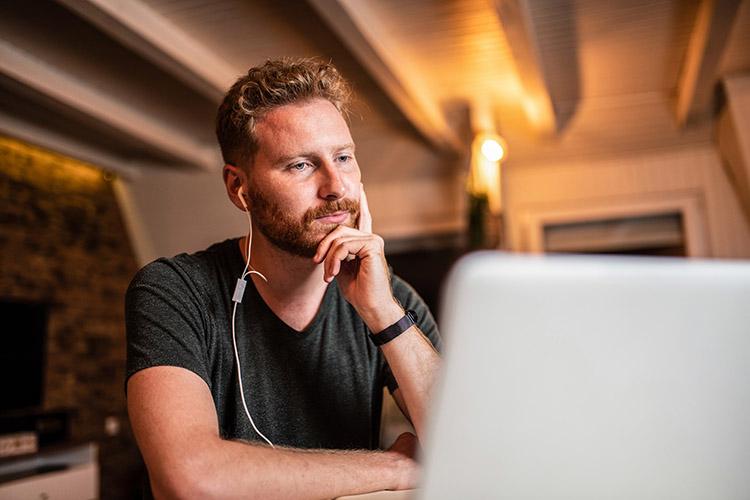 Mann mit Köpfhöhrern nachdenklich vorm Laptop.