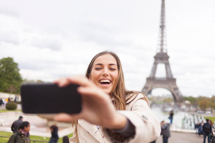 Frau macht Selfie von sich vor dem Eiffelturm.