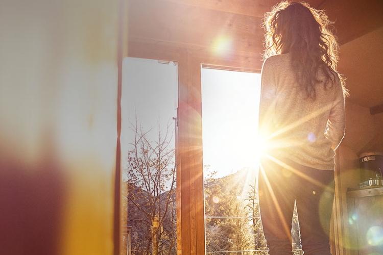 Frau steht vor der Wohnzimmertür, durch die die Sonne scheint