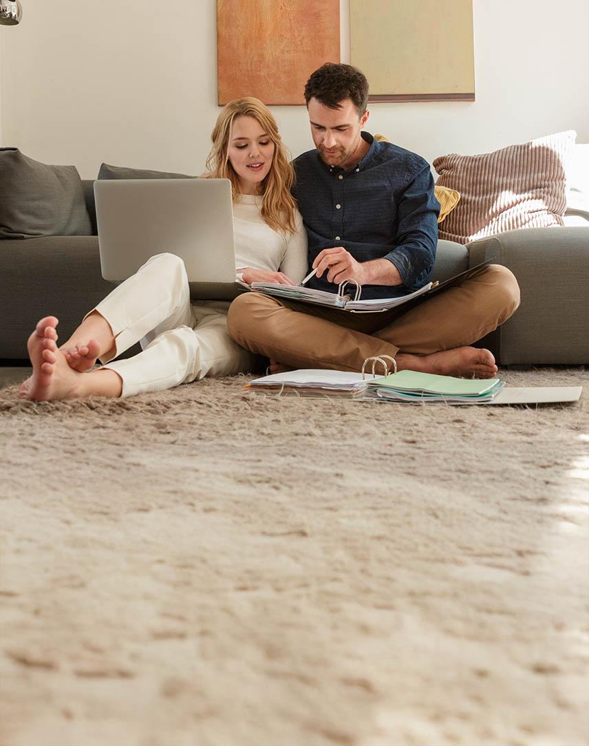 Ein junges Paar sitzt mit Aktenordner und Laptop auf dem Boden vor der Couch