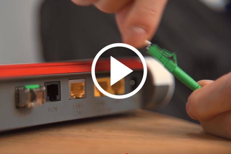 Eine Hand hält ein grünes Kabel, das mit einem Router verbunden wird