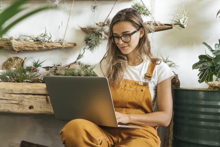 Ein junges Paar sitzt mit seinem Hund auf der Couch und schaut etwas im Laptop nach