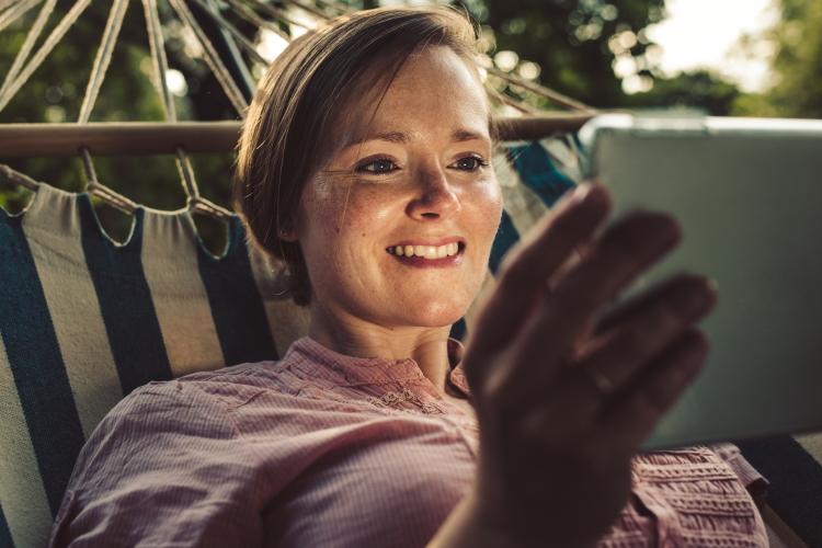 Frau in Hängematte liegend schaut aufs Tablet.